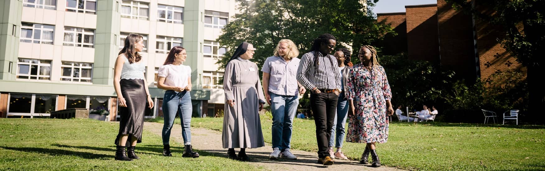 Diverse Menschen gehen nebeneinander und sind im Gespräch. Im Hintergrund das Vinzenzkrankenhaus Hannover.