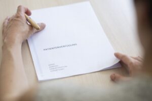 Auf dem Tisch liegt eine Patientenverfügung, es sind Hände zu sehen, die die Verfügung halten